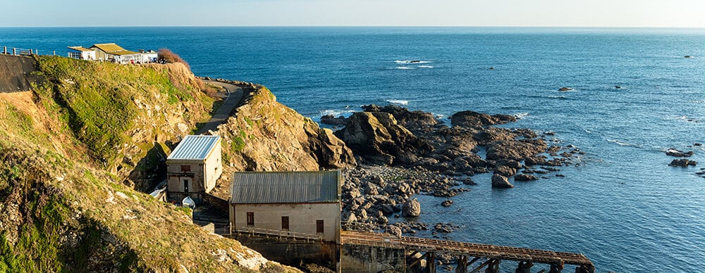 dog friendly beach cafés in Cornwall : Lizard Point showing Polpeor Beach Cafe on the cliff edge